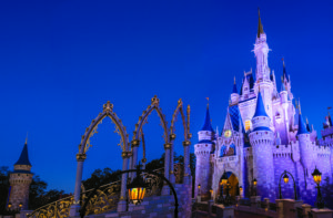 Picture of Cinderella's Castle at dusk with yellow lights, gold points, arches that have a decorative arch in gold, at Magic Kingdom