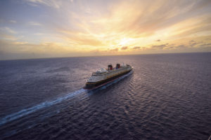 Disney Cruise Line Ship, sailing in open waters with a sunrise picture with cloud cover, blue waters, black bottom of the cruise ship, two funnels, yellow lifeboats