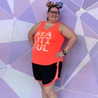 picture of Charlotte Strickland with a purple geometric background wearing a bright orange color shirt, black pants with orange trim and a pair of minnie ears