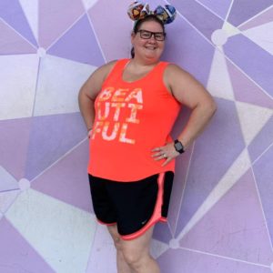 picture of Charlotte Strickland with a purple geometric background wearing a bright orange color shirt, black pants with orange trim and a pair of minnie ears