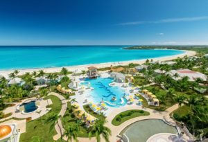 Sandels Emerald Bay with a caribbean sea in the background, Pool that has blue Letters in saying Sandals, lush green grass and palm trees along with cabanas for couples to lounge in