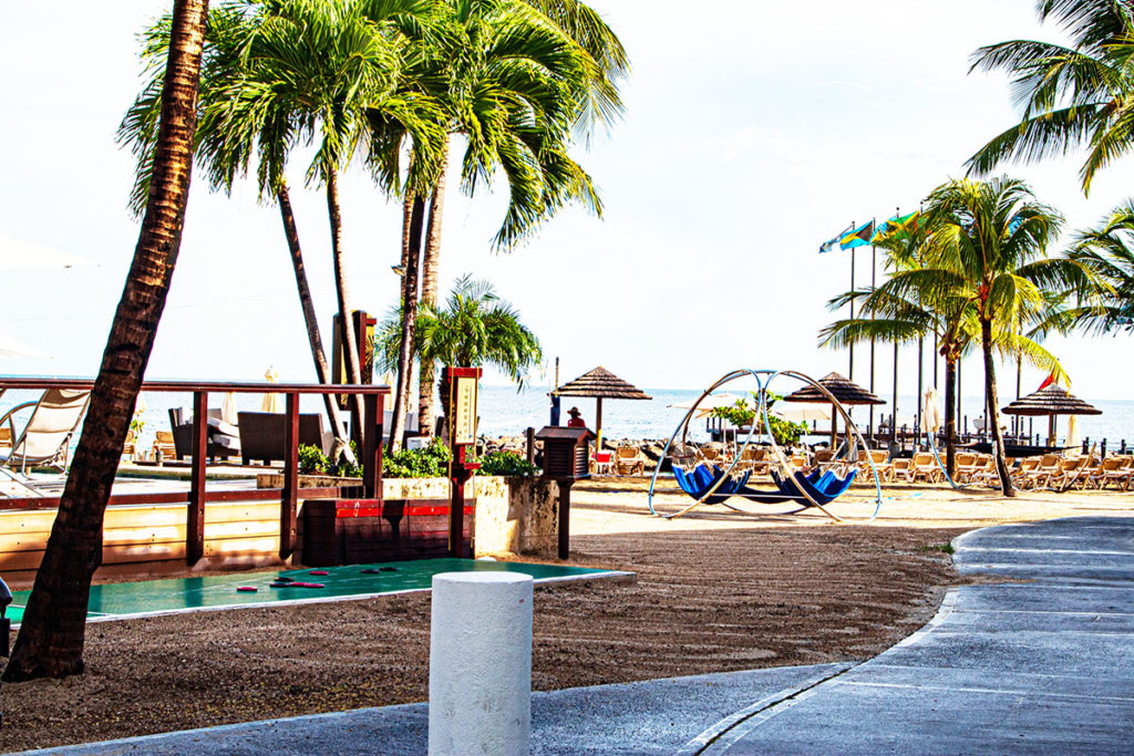 The beach area walkway showing hammocks to relax in, shuffleboard, the ocean and palm trees with different flags fying